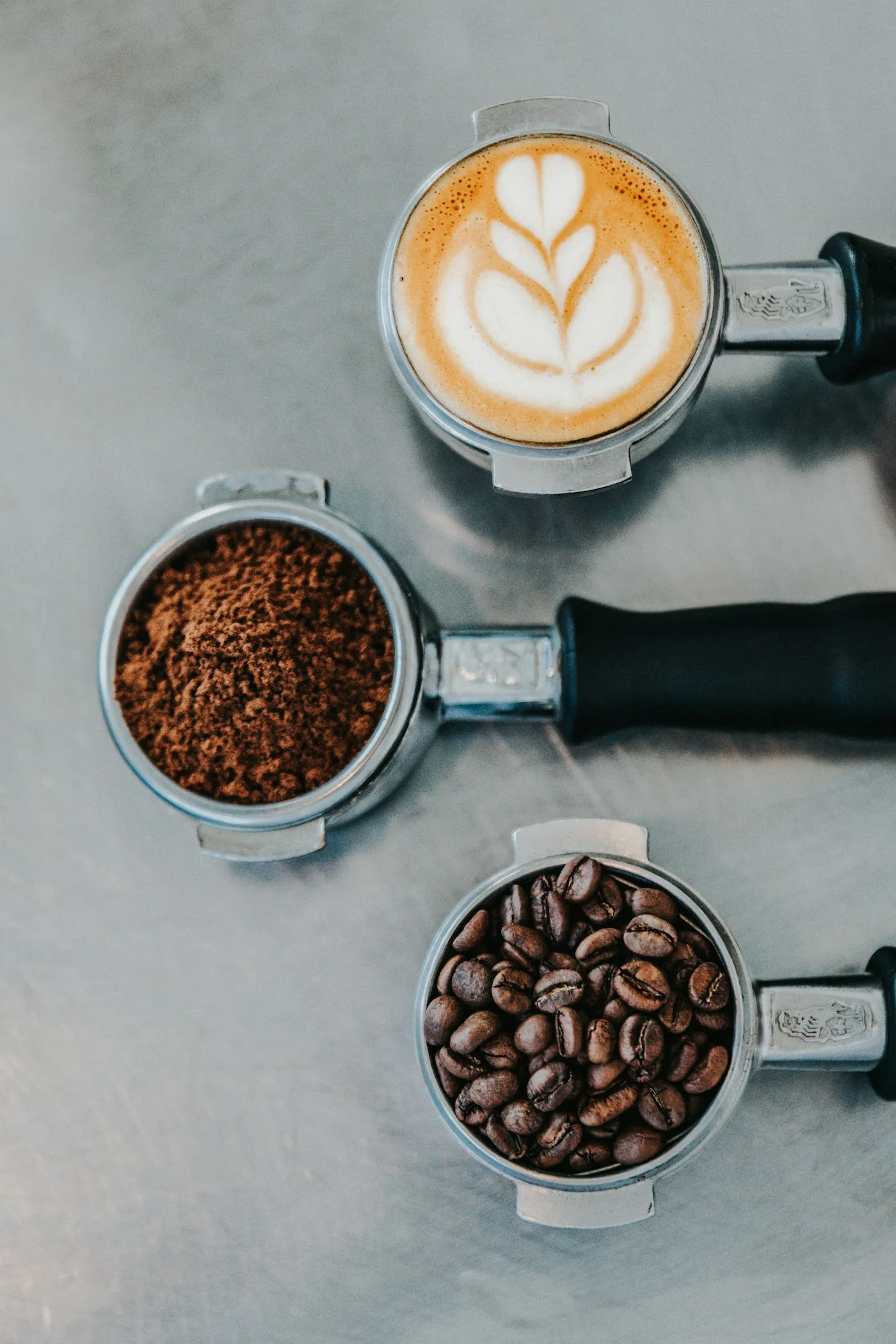 A portafilter of ground coffee beside another holding whole roasted beans