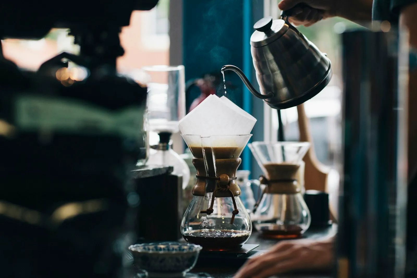 A barista pouring hot water from a gooseneck kettle over a paper filter in a pour-over brewer